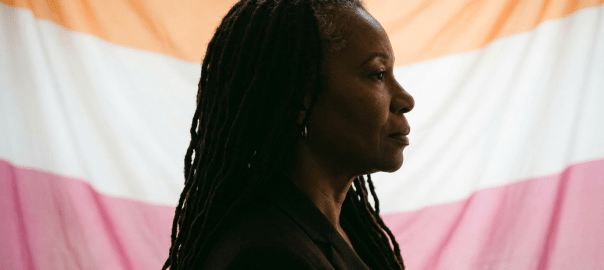 Woman standing in profile in front of a multicolored inclusivity flag